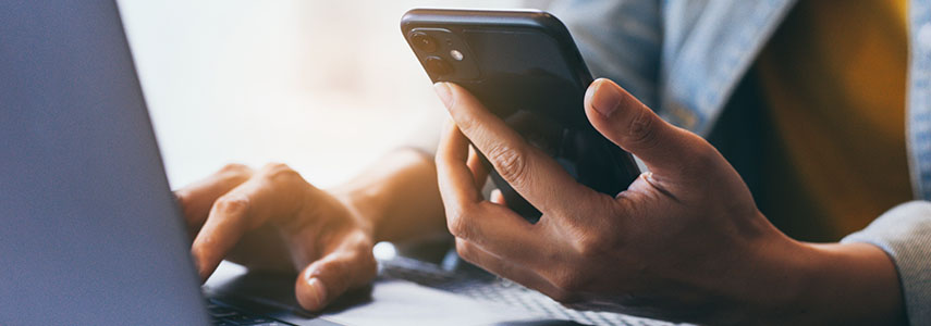 photo of a person on a computer with a phone in their hand