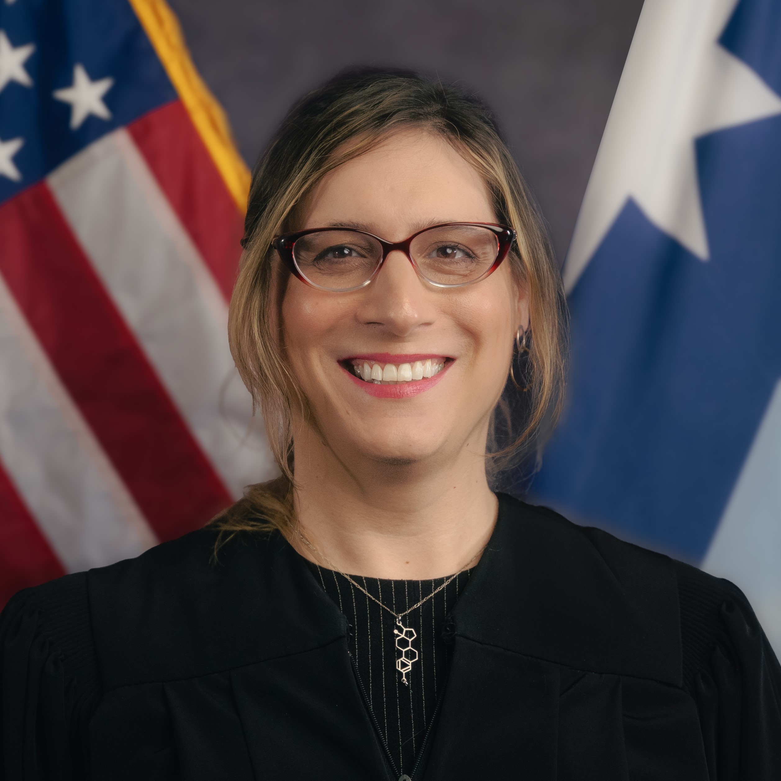 An image of a woman (Judge Christa Moseng) in a judges' robe standing in front of a U.S. flag and a State of Minnesota flag. 