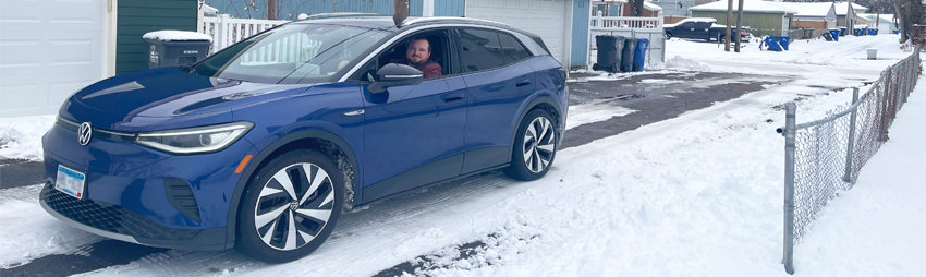 a man drives a Volkswagen ID.4 down a snowy alleyway behind houses