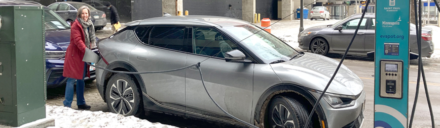 A woman in a red coat plugging her EV in to a street-side charging station