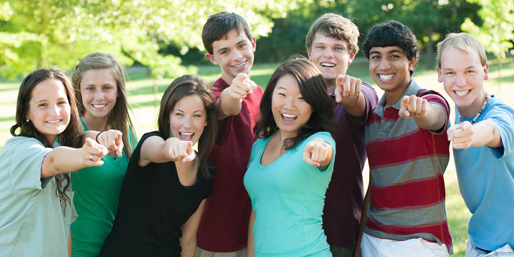 a diverse group of children smiling and pointing at the camera