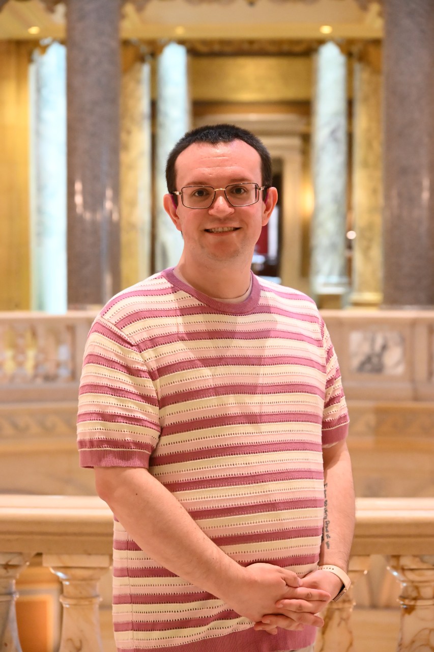 Smiling person with glasses standing within the Minnesota State Capitol