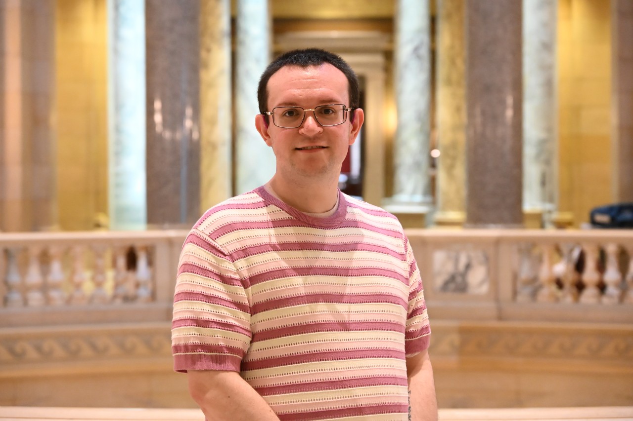 Smiling person with glasses standing within the Minnesota State Capitol
