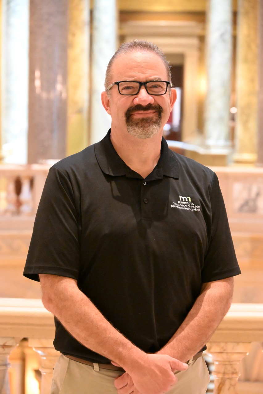 Smiling person with glasses standing within the Minnesota State Capitol
