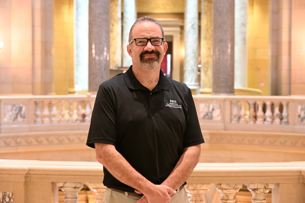 Smiling person with glasses standing within the Minnesota State Capitol