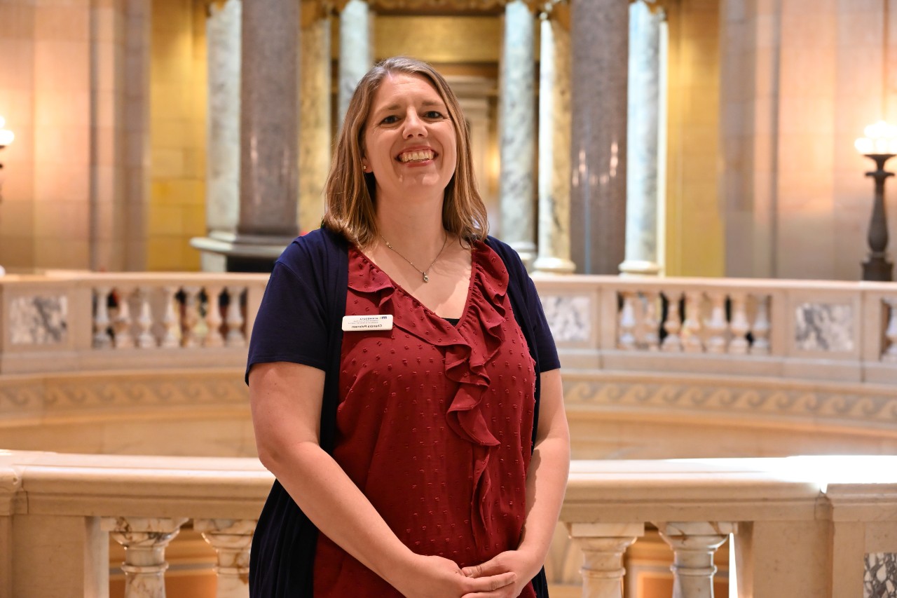 Smiling person with blonde hair standing within the Minnesota State Capitol