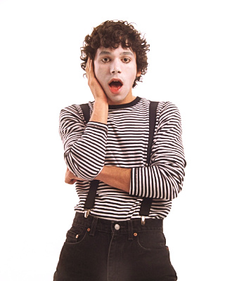 Kyle, dressed as a mime with black and white striped shirt and black pants supported by black suspenders, with his face painted white, holds a dramatic pose with a surprised look on his face. 