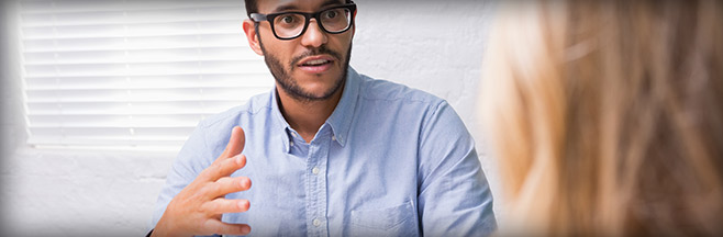 Man with glasses in blue shirt in conversation with blond-haired woman