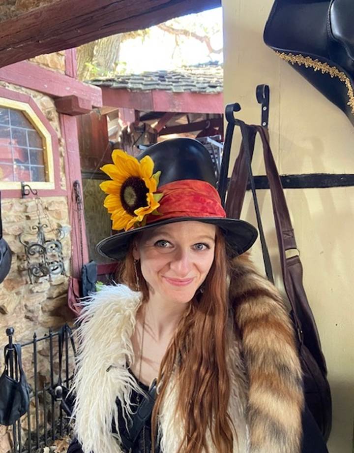 Fun snapshot of Elizabeth as she wears a top hat with a red band and a sunflower pinned to it, a white boa around her shoulders.