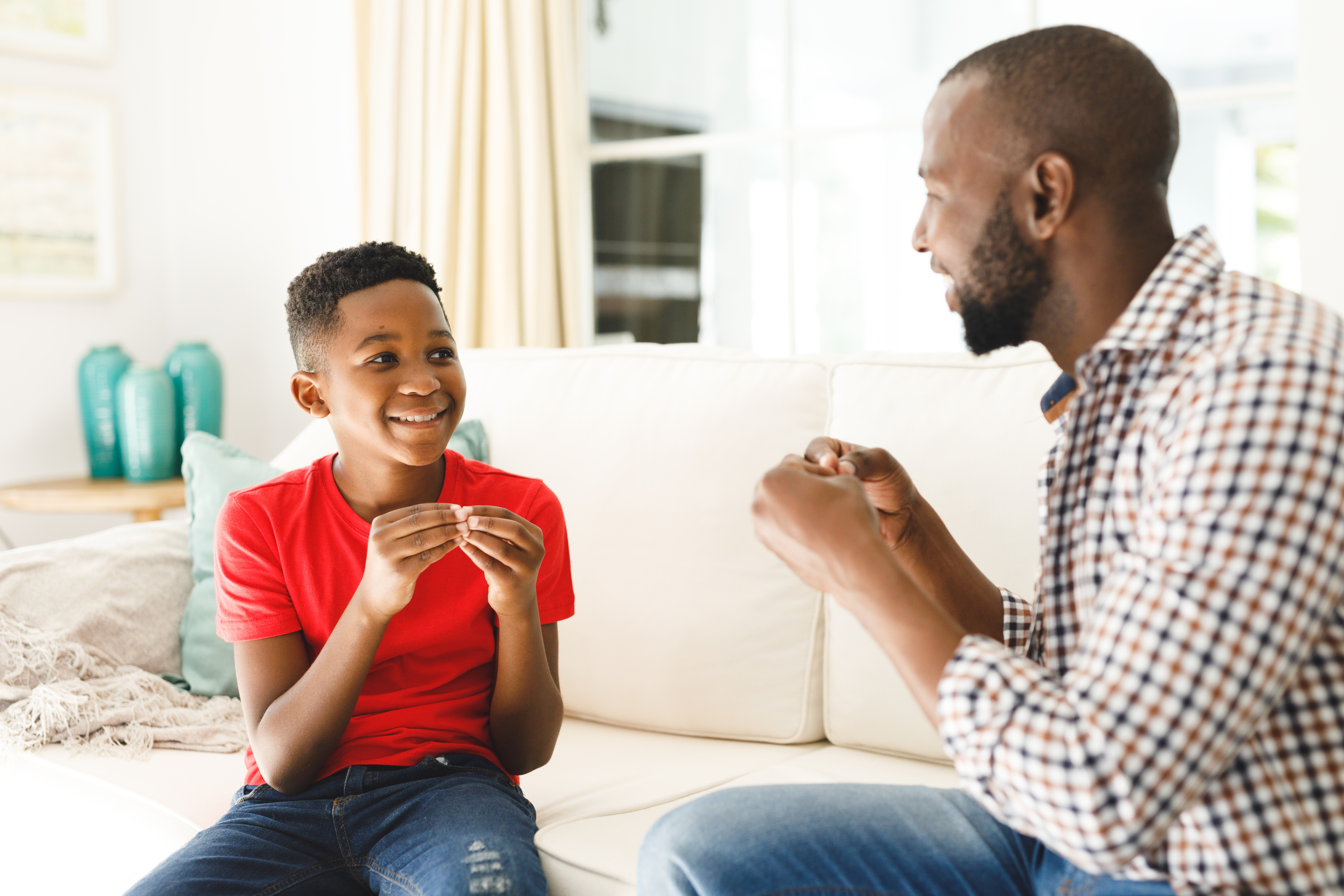 A father and his son are sitting on a couch chatting in American Sign Language.