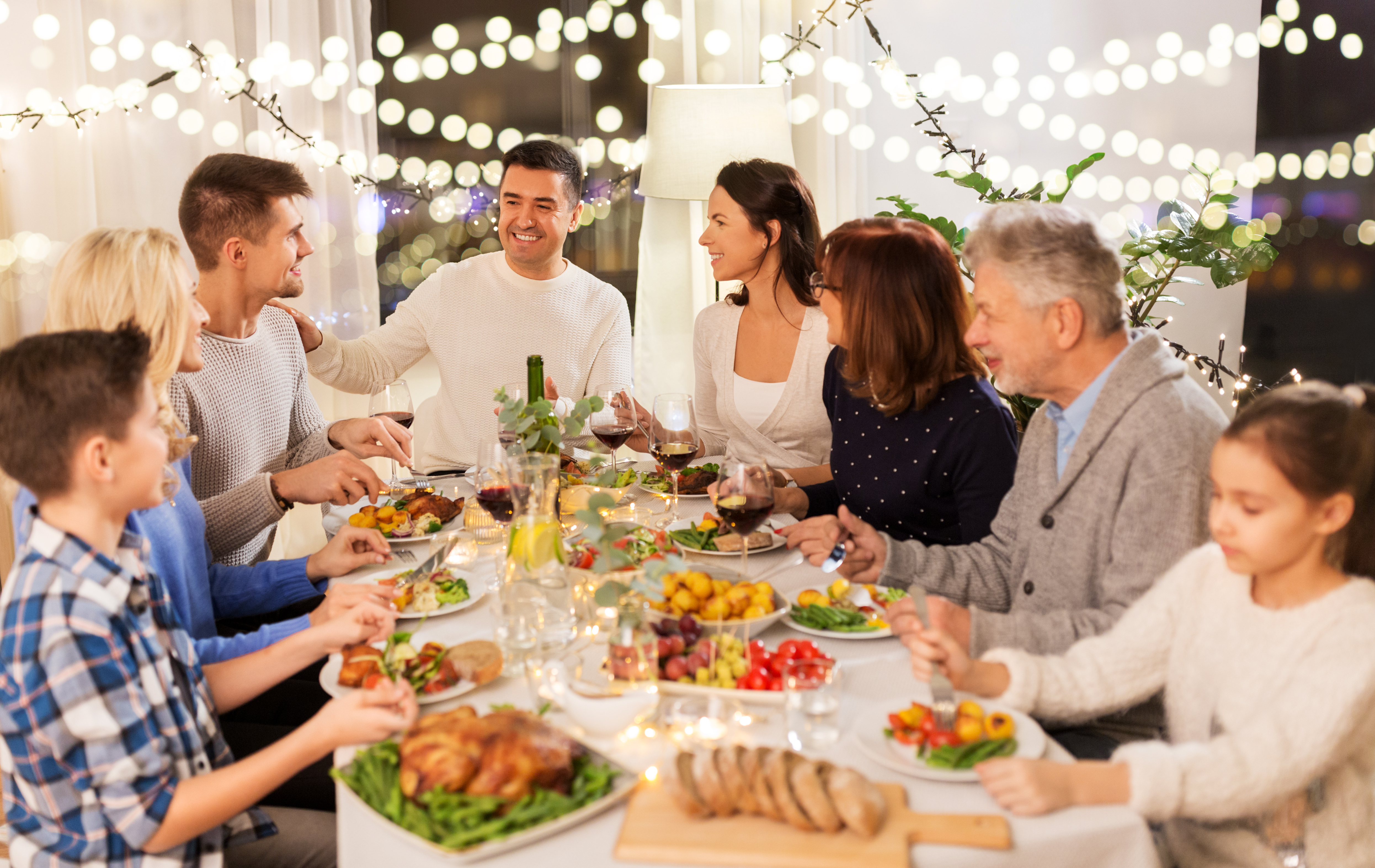Three generations of family seated at a table for dinner. The table is well-lit with bright string lights. 