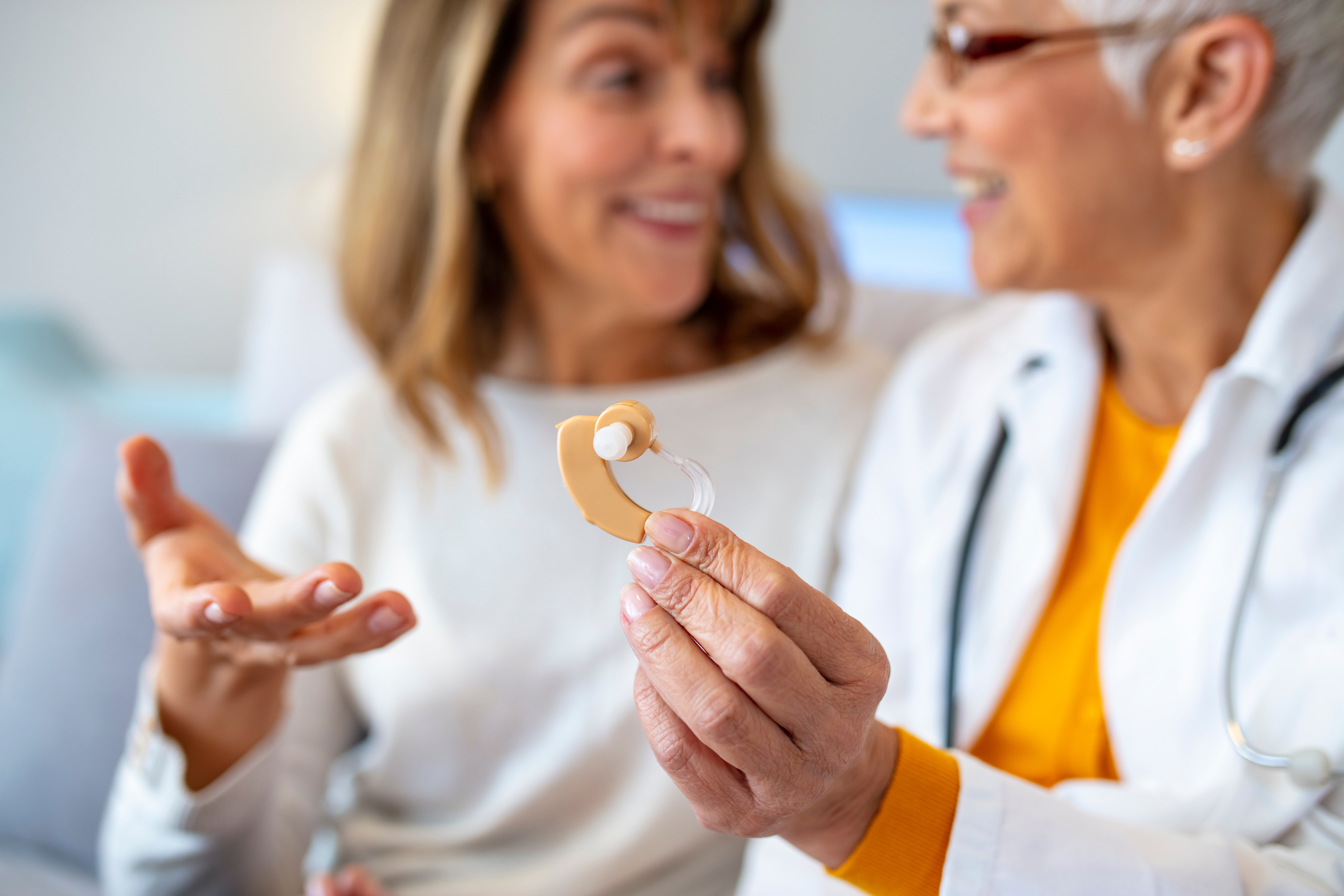 An audiologist showing another woman a hearing aid.
