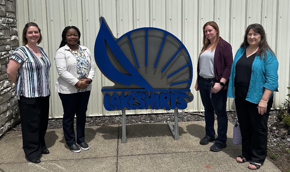 Four women stand around the Lakeshirts LLC logo
