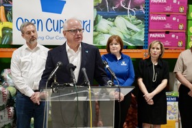 Governor Walz stands behind a podium, speaking to an unseen crowd. DEED Commissioner Varilek stands behind him, as well as two women.