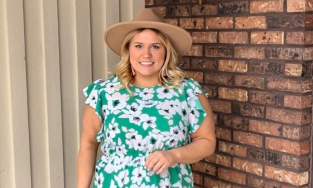 Woman stands in front of a brick wall smiling for picture.