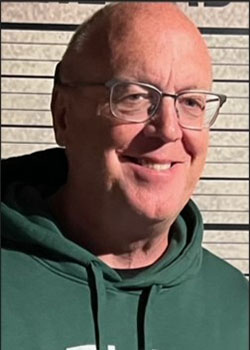 A man in a green hoodie smiles in the morning sun.