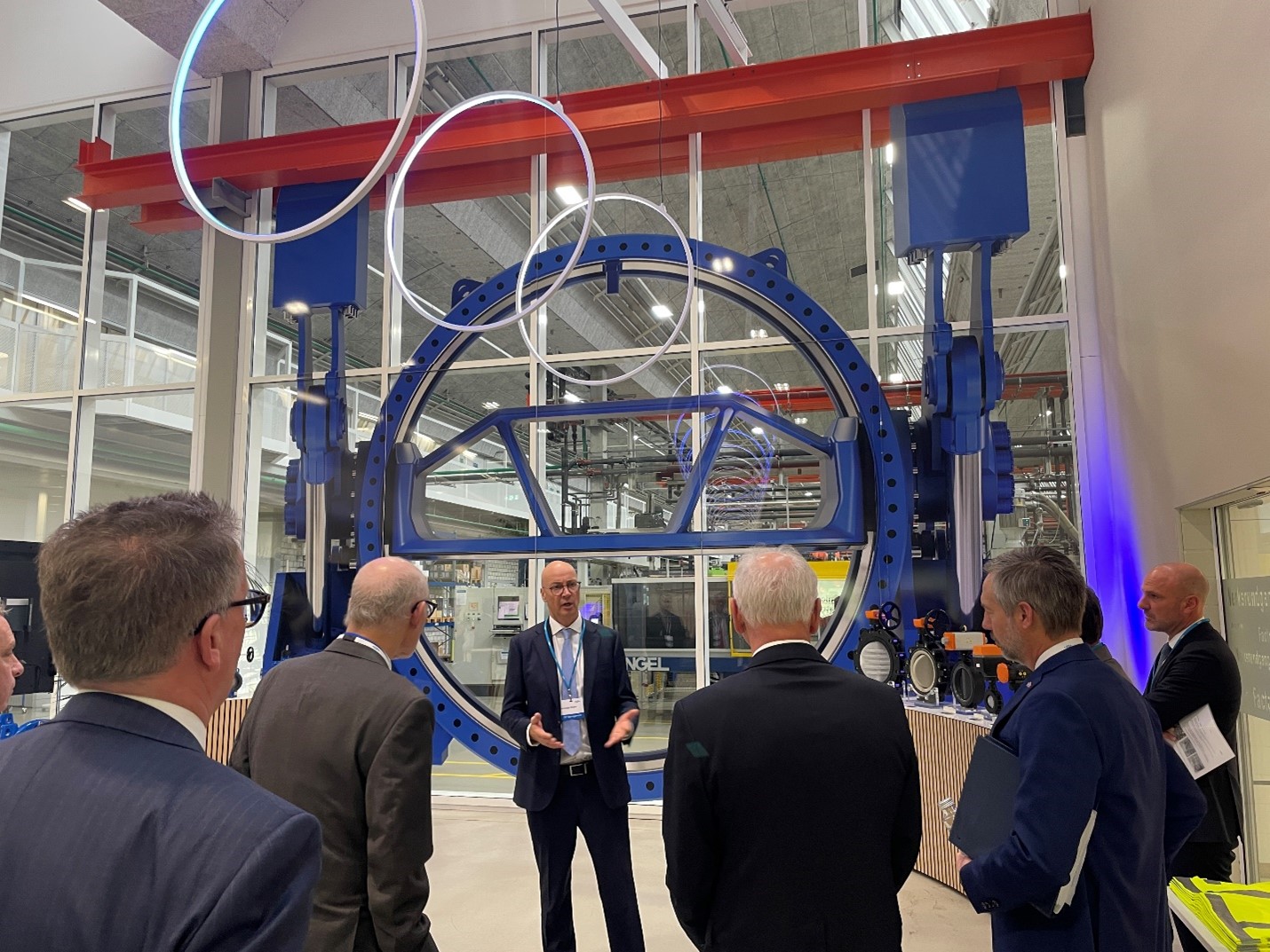 Governor Walz, Commissioner Varilek and two others have their back to the camera, listening to a man speaking in front of them.