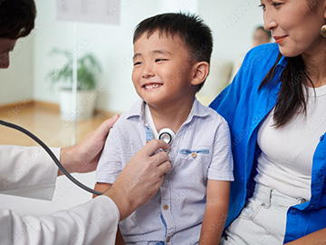 Smiling boy looking at doctor listening to his breath, visiting pediatrician