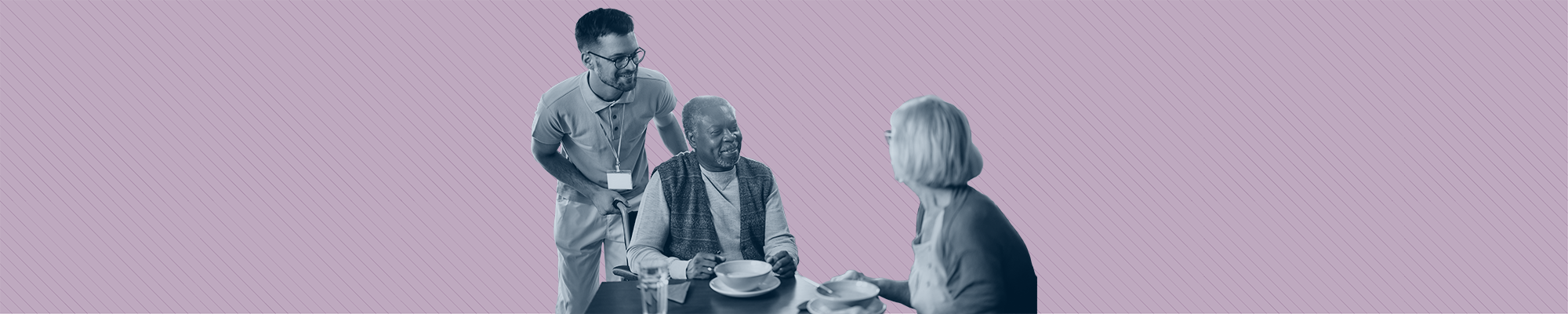 A care worker laughs with two elders who are eating breakfast.