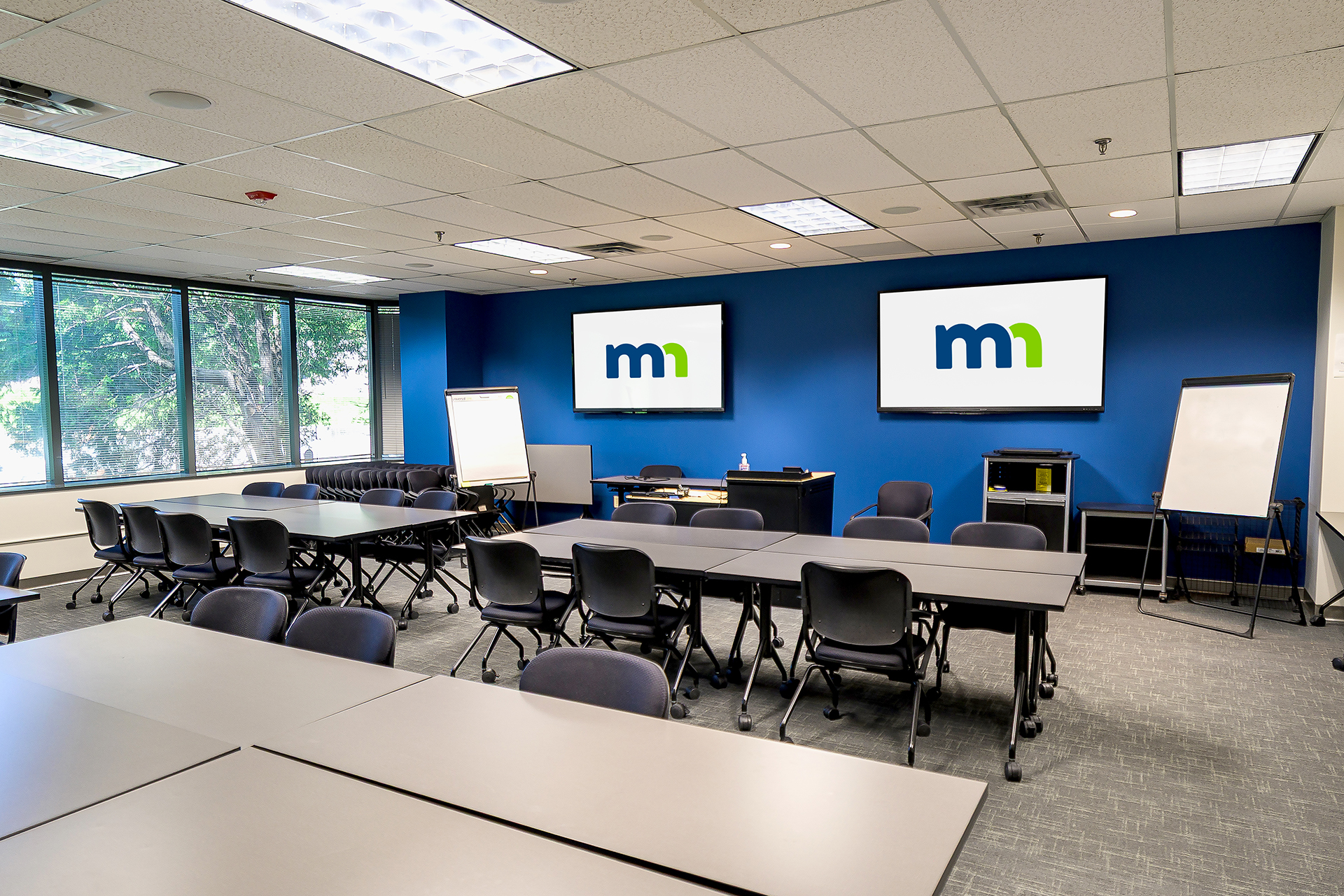 Socrates room at the Training Center with a front lectern, several tables, and two TVs for presentations