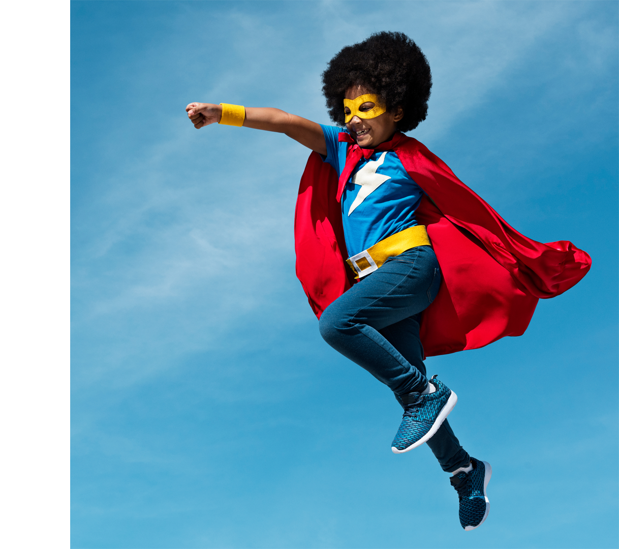 A young person wearing a hero cape and mask flying through the air