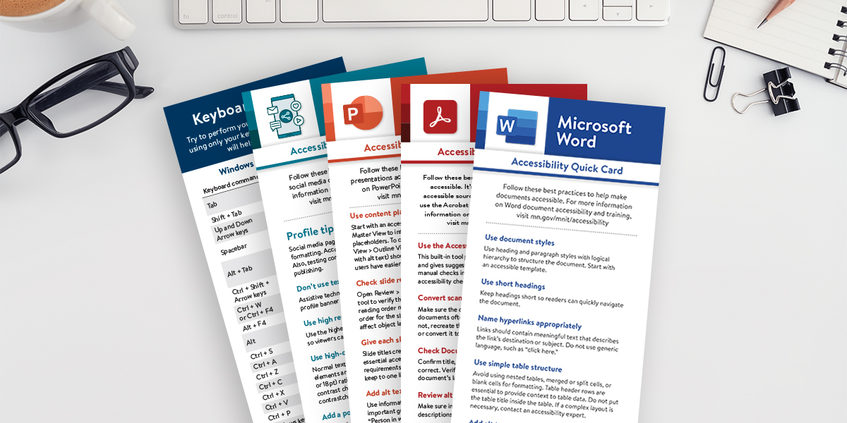 A set of five accessibility quick cards are laid out on a desk with a keyboard, glasses, and a notebook in the background. The cards are designed for different software programs, including Windows, Microsoft PowerPoint, Adobe Acrobat, and Microsoft Word. Each card has its own color-coded header, with icons representing the respective programs (keyboard icon for Windows, PowerPoint logo, Acrobat logo, and Word logo).