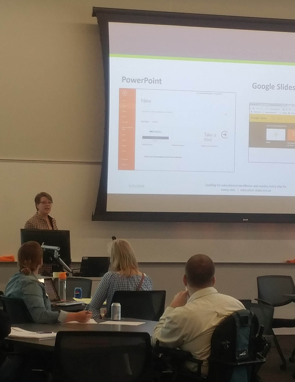 Kursten Dubbels at podium next to large screen showing images of PowerPoint and Slides.
