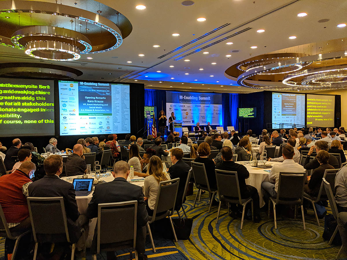 View of main ballroom at M-Enabling, showing two full-size captioning screens alongside separate slide screens.