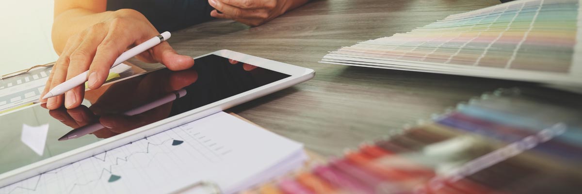 A person at a table working on a digital tablet next to color swatches.