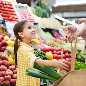 Child putting vegetables into a basket at the store