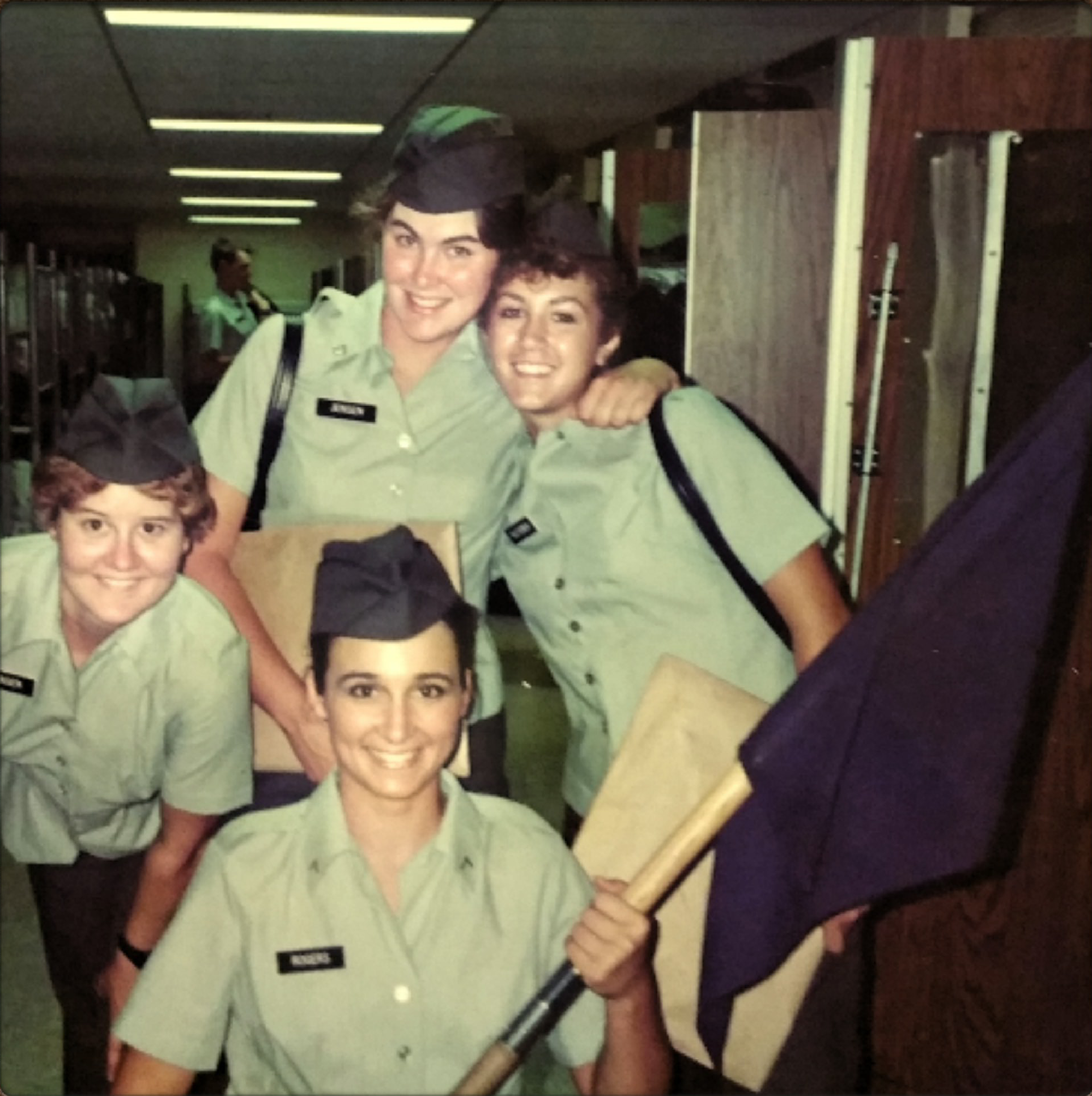 Group of four women in uniform smiling and holding a blue flag.