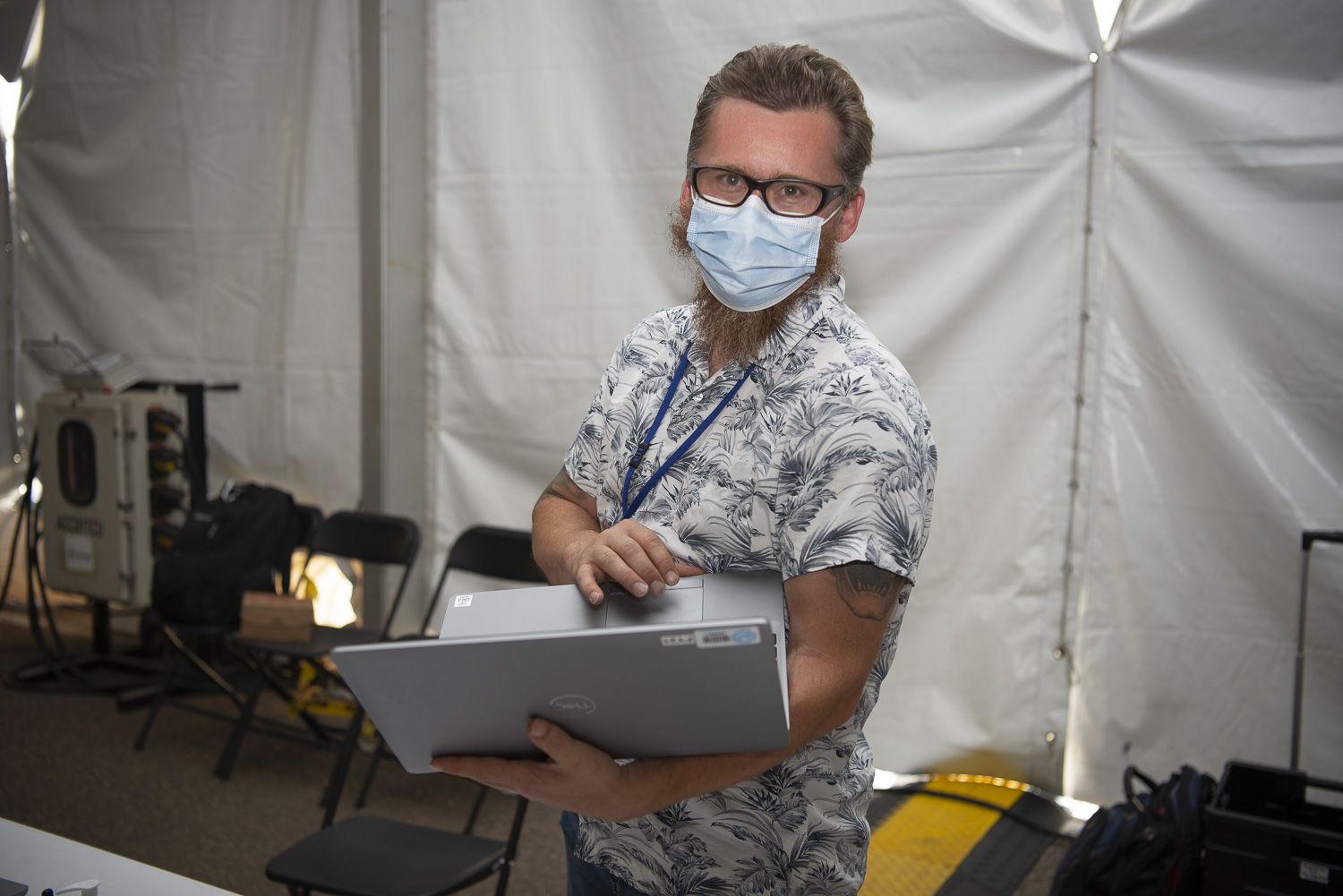 Andrew Schuster wearing a mask while holding a laptop.