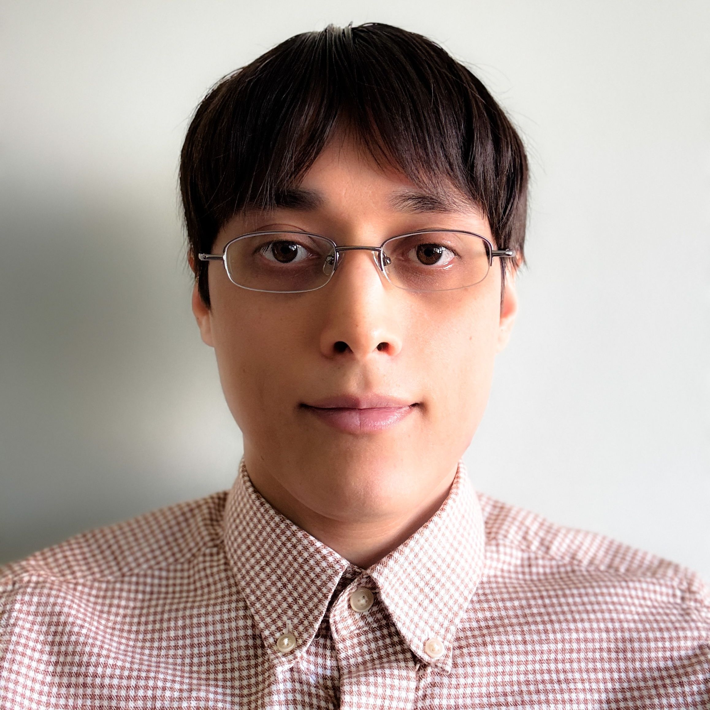  Abraham has tan skin, dark hair, and wears glasses. They are wearing a light colored checkered button up shirt.