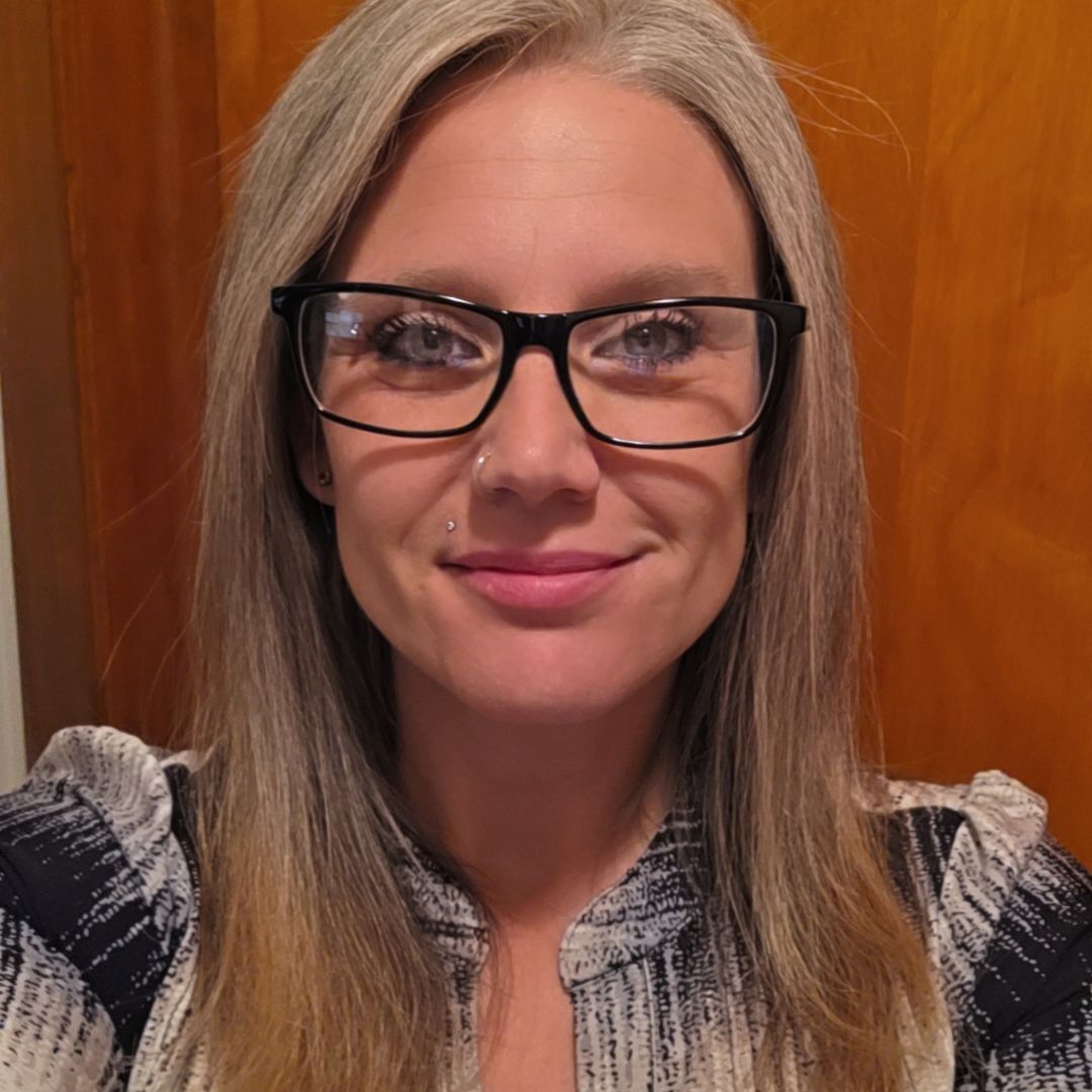 Angela is a woman with light skin, long blonde hair, and glasses.