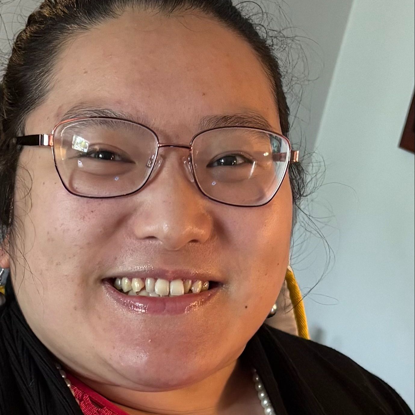Mao is a Hmong American woman with dark hair pulled back. She is wearing glasses, a black sweater, and pearl jewelry. 
