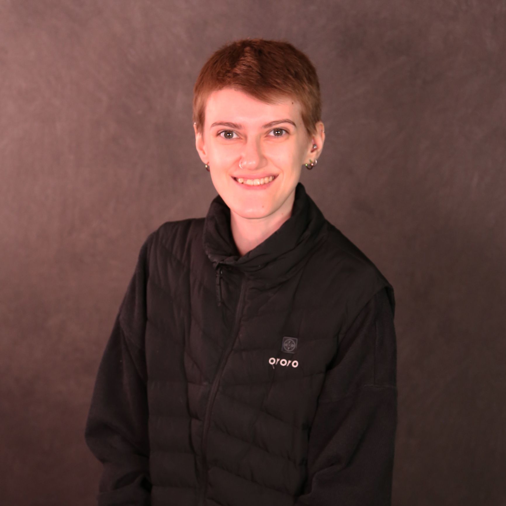 Riss is a white non-binary person with short hair and earrings. Riss is wearing a black jacket.