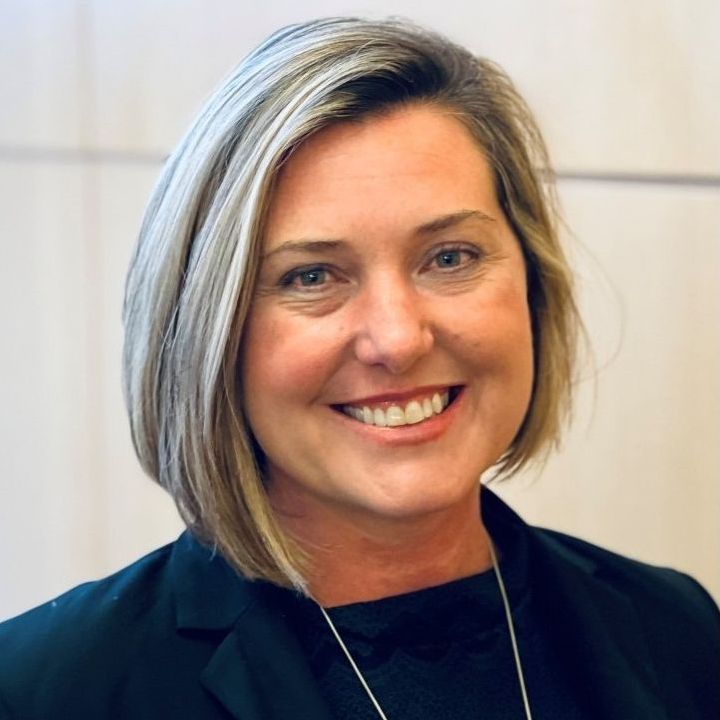 Natasha is a white woman in her forties with a blonde bob. She is wearing a black shirt and jacket and is smiling.