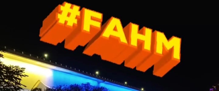 A bridge lit up in blue, white, and yellow, with #FAHM superimposed in the sky, for Filipino American History Month