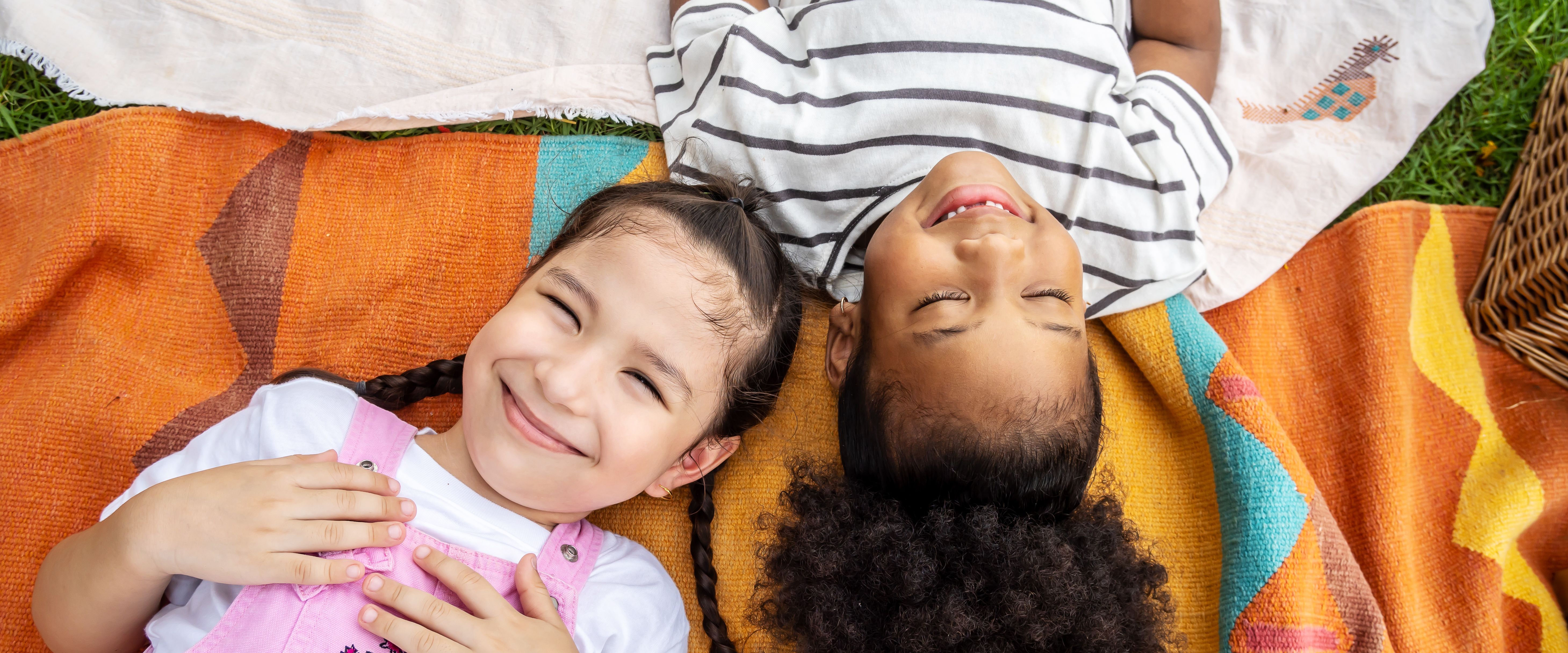 Two girls lying on picnic blankets and smiling.