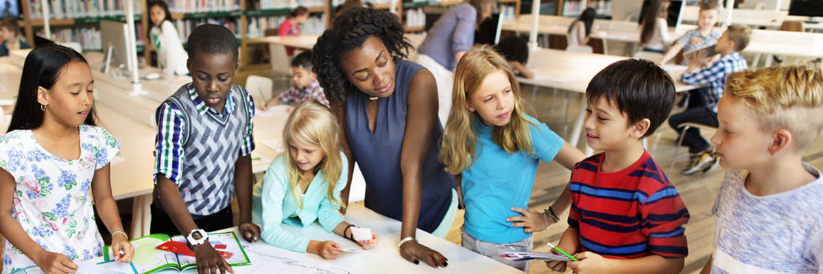 Una maestra de pie junto a una mesa con su alumnado