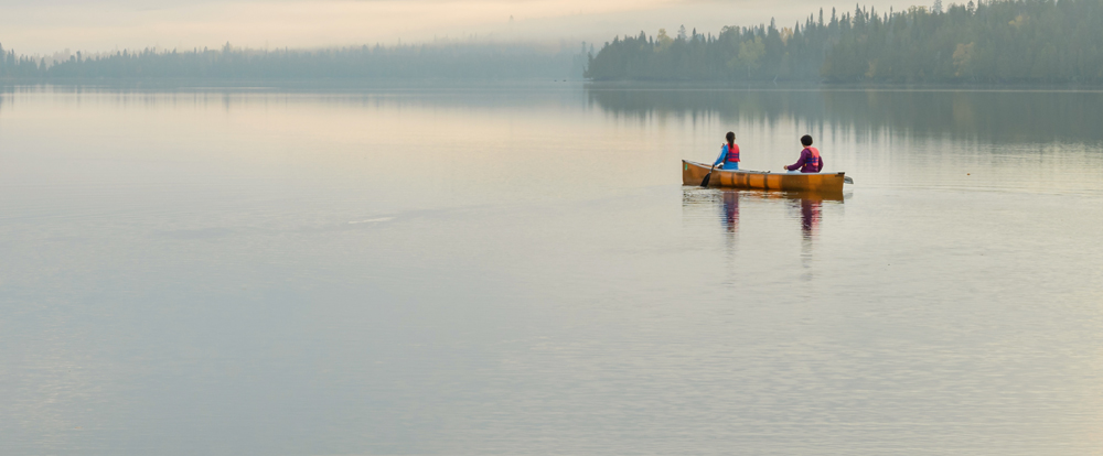 Two people canoeing on a lake away from the camera in the fog
