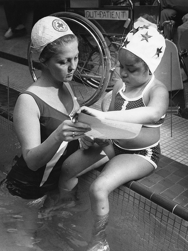 Photo of an adult woman and a female child at an indoor swimming pool, both wearing swimming caps