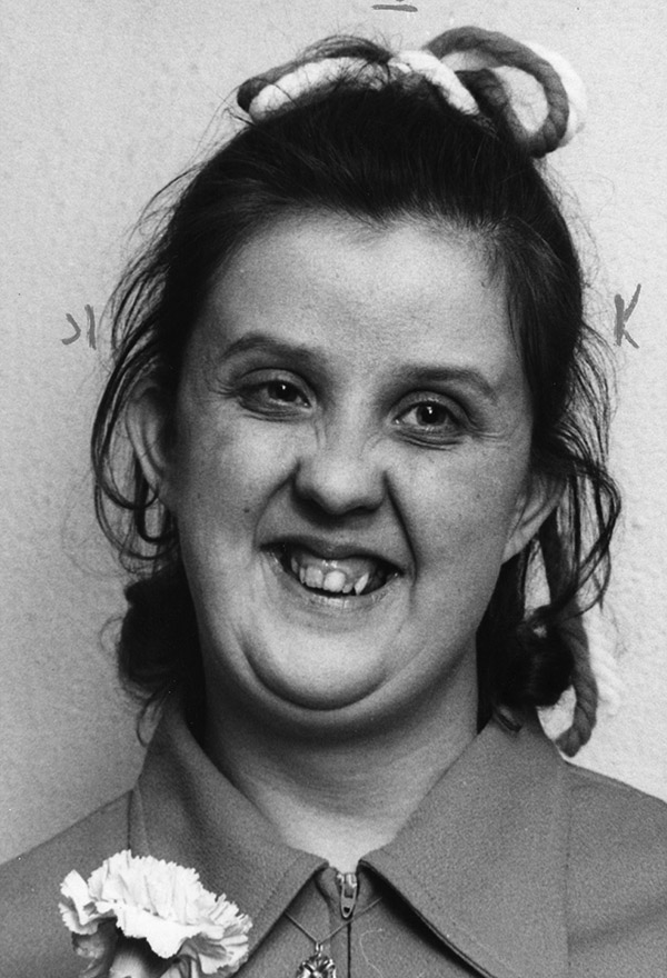 Photo of a smiling woman with a bow in her hair and a carnation on her suit jacket