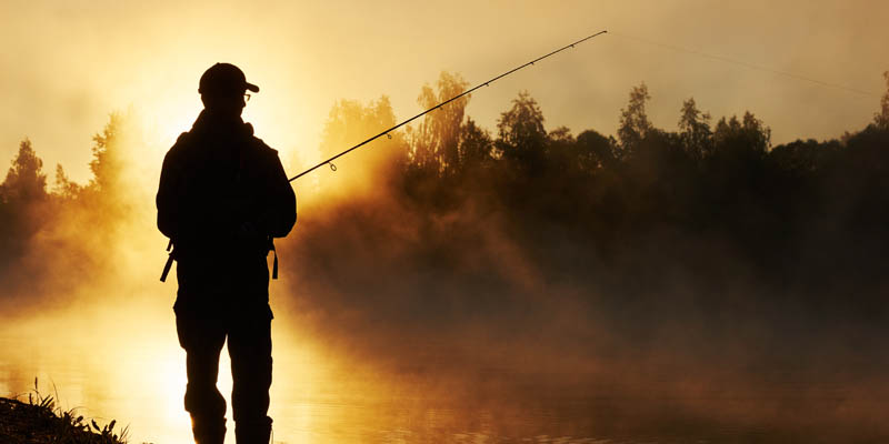 A man fishing from the shore of a lake.